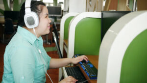 A woman using a computer with headphones and a Braille display, representing digital accessibility and inclusive technology.